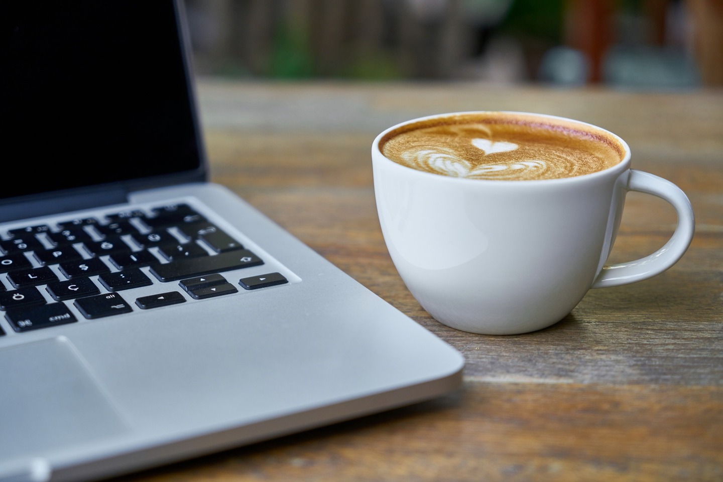 Cup of coffee next to a laptop on a table with an unfocused background