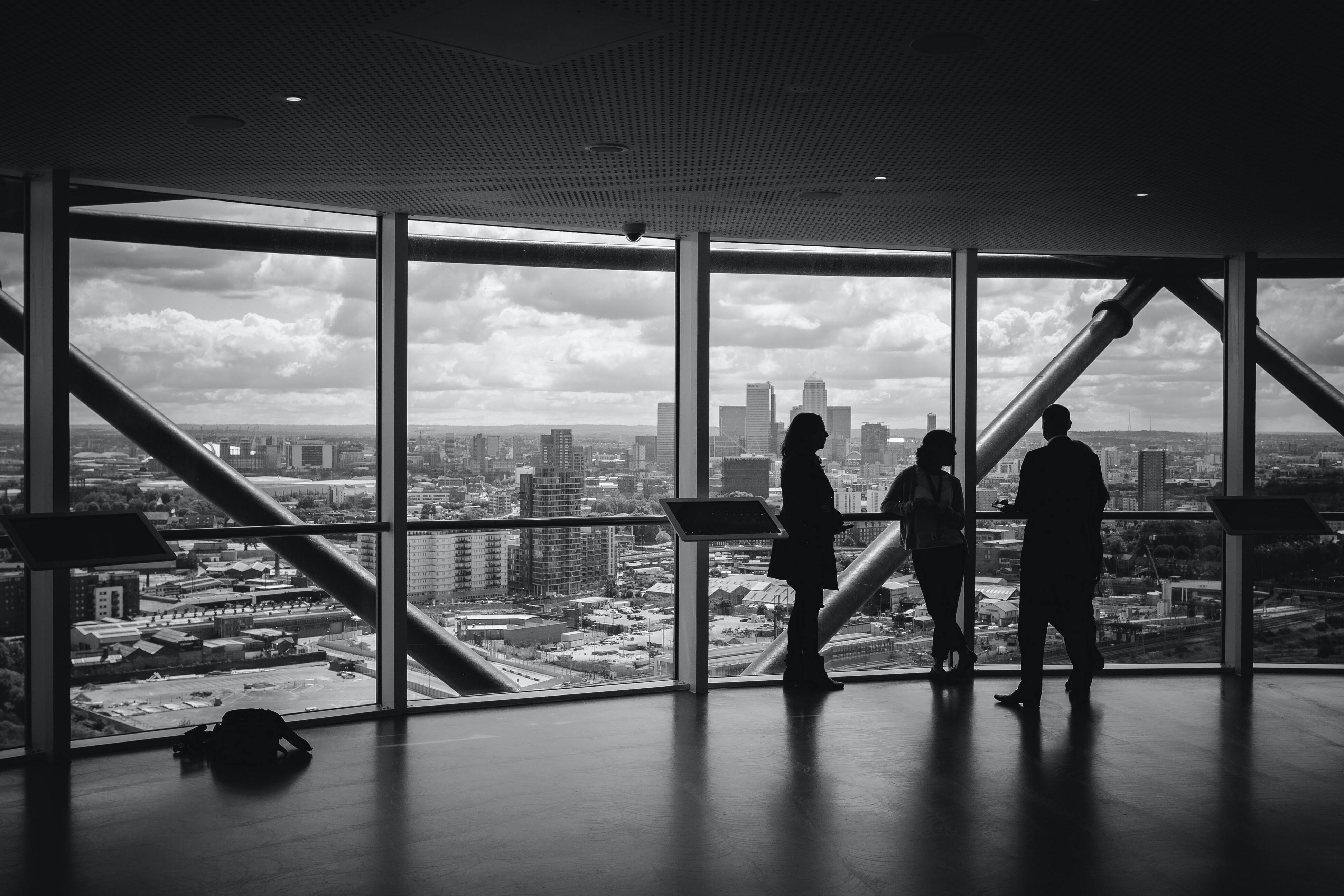 Three person talking in a building with a city view in the background