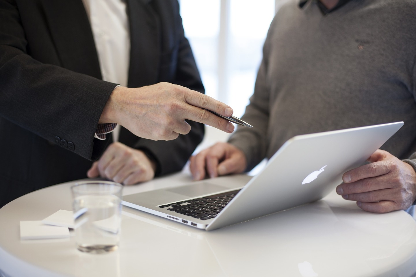 Two person speaking and one of them pointing a computer with a ballpoint