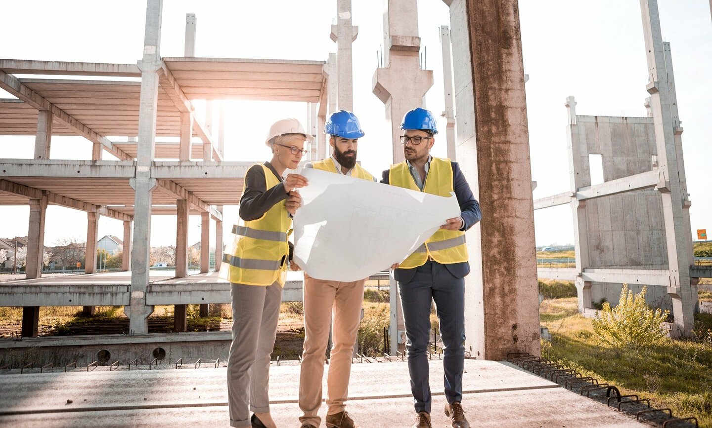 Three person wearing workwear watching a blueprint in a construction site