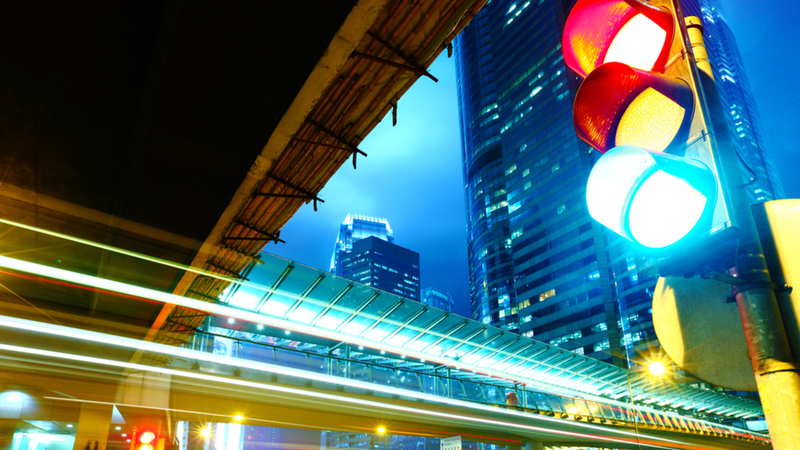 Traffic light on a road with moving lights with buildings in the background